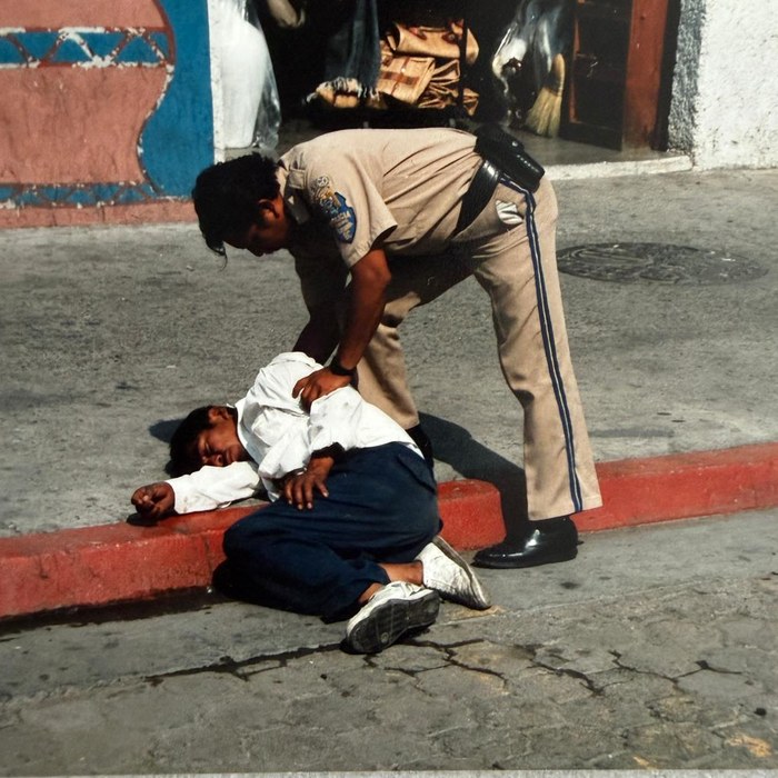 Tijuana, 1991: a police officer bends over a man lying on the red curb