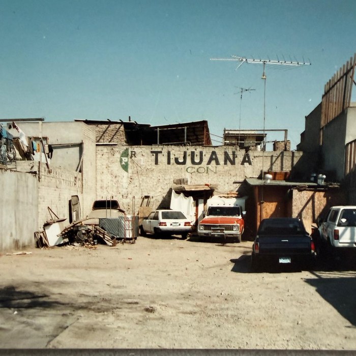 Backyard in Tijuana, 1991: brick wall with the word Tijuana, old cars in front